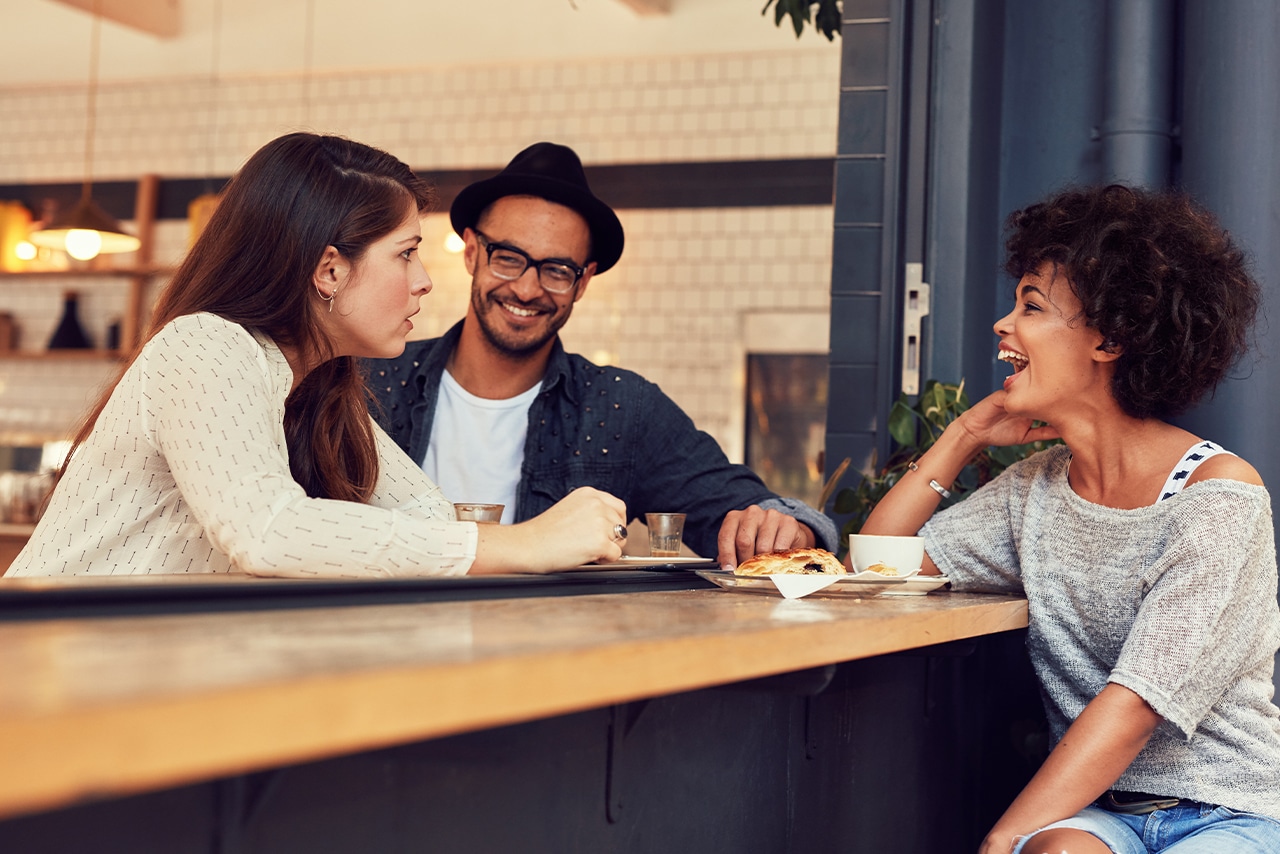 Two young women and a young man enjoying a conversation and hanging out at a cafe as an example of a self-care practice